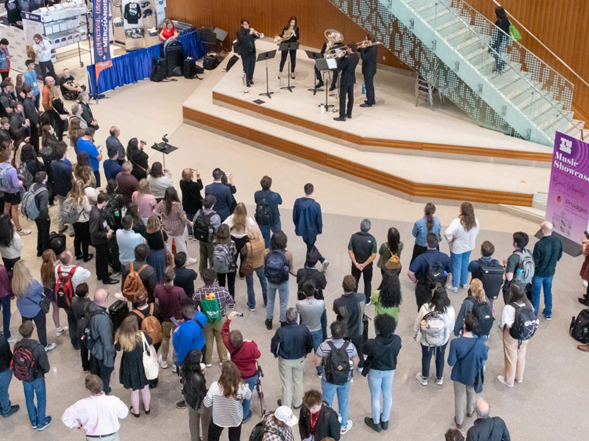 A crowd of people stand in a large open lobby watching a small group of musicians perform